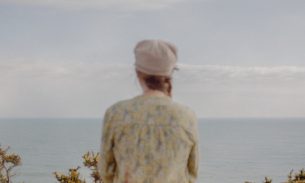 An anonymous woman with her back to the camera looks over the coastline