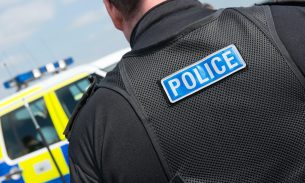 A police officer moving towards a police jeep on a sunny day. Image only shows the police officer’s shoulders and neck from behind