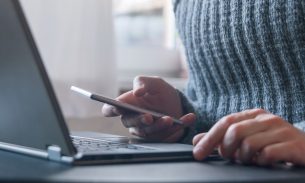 A man uses his phone to access an account on his laptop with two-step verification